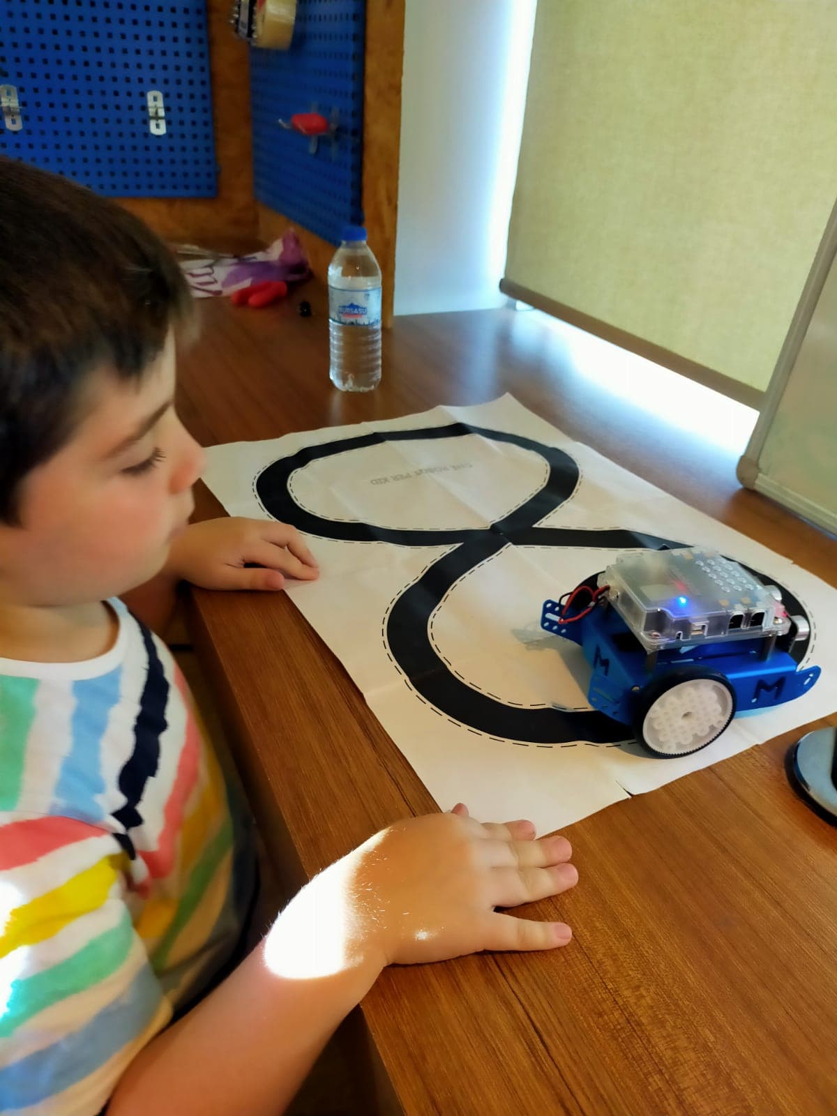9 yaşındaki bir öğrenci, 8 şeklindeki siyah çizgi pistinde mavi mBot robotunu izliyor