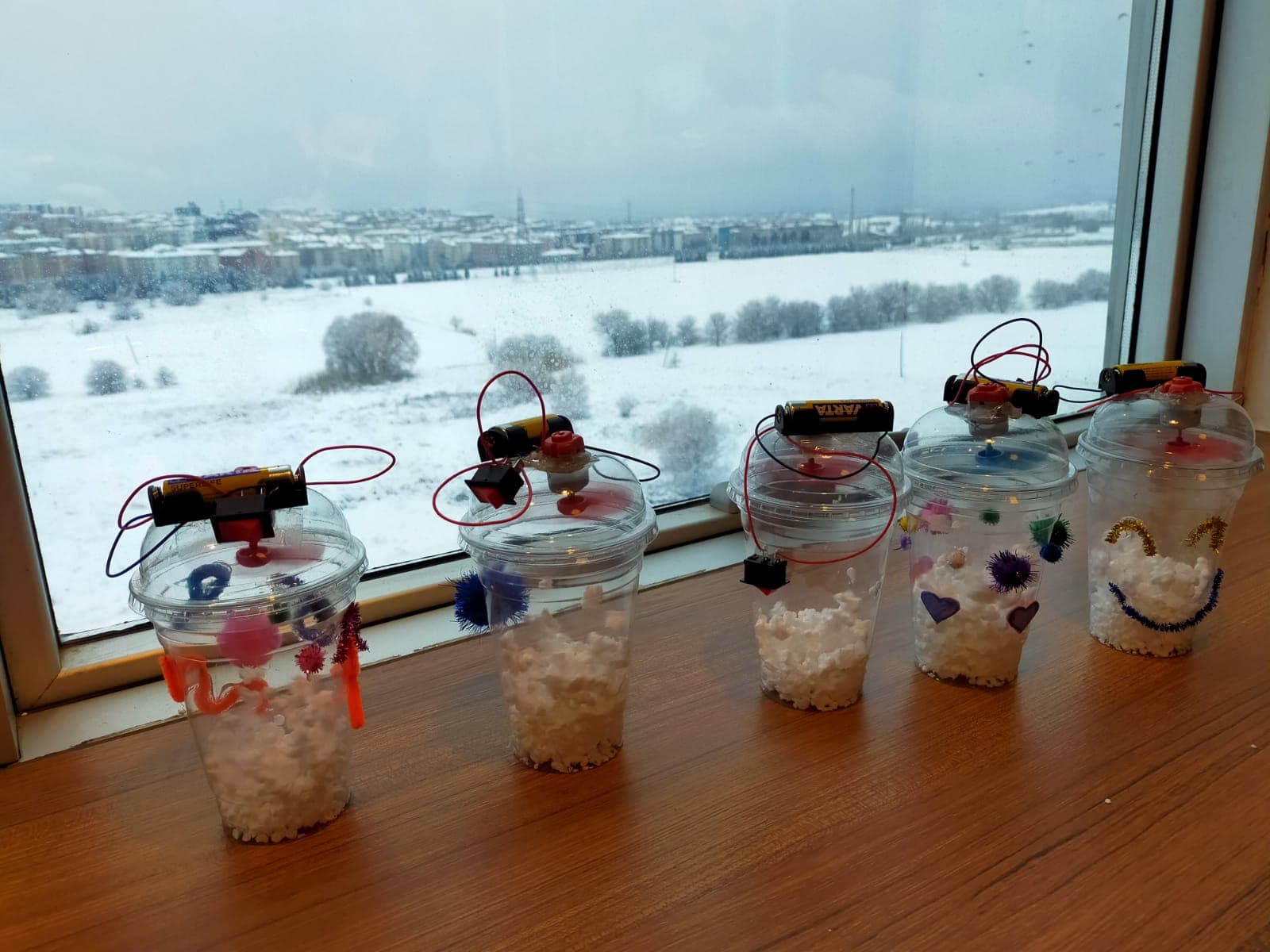 Karlı pencere önünde dizili, pille çalışan ışıklı el yapımı elektronik kar küreleri