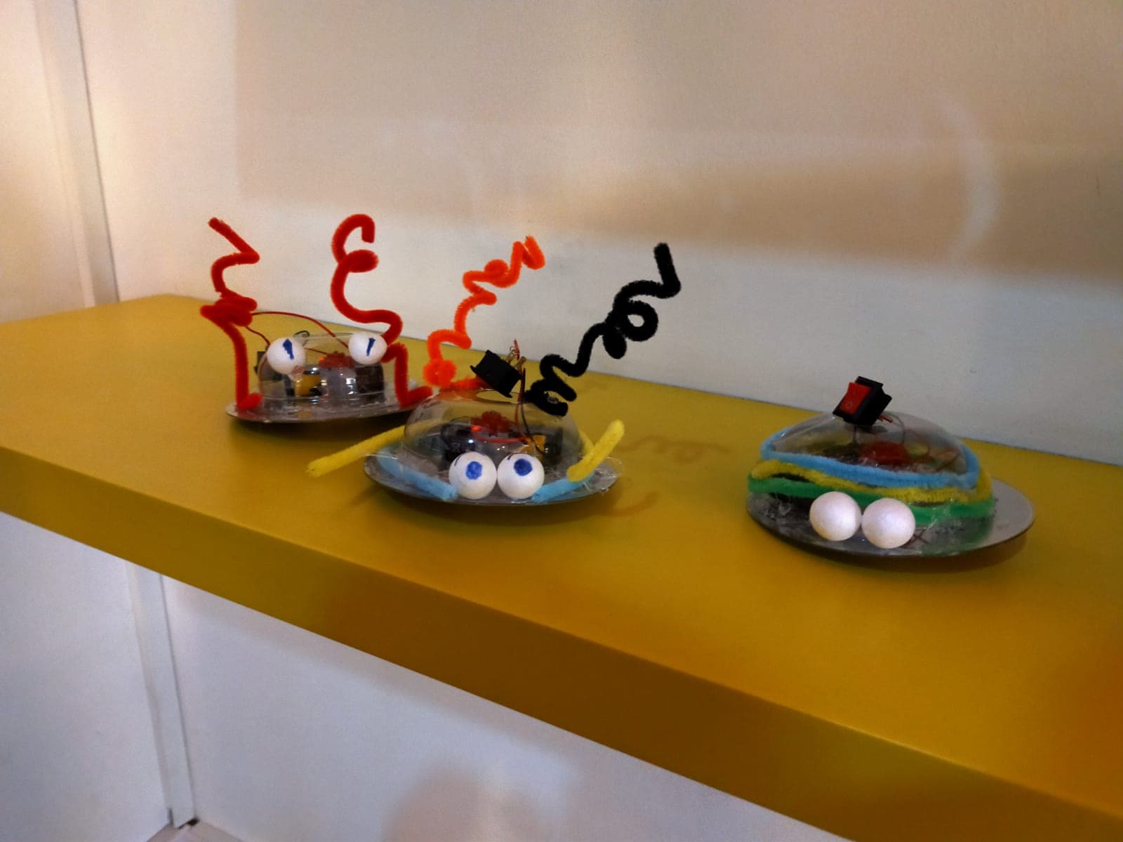 Renkli pipe-cleaner ve gözlerle süslenmiş, titreşimle yürüyen üç küçük robot